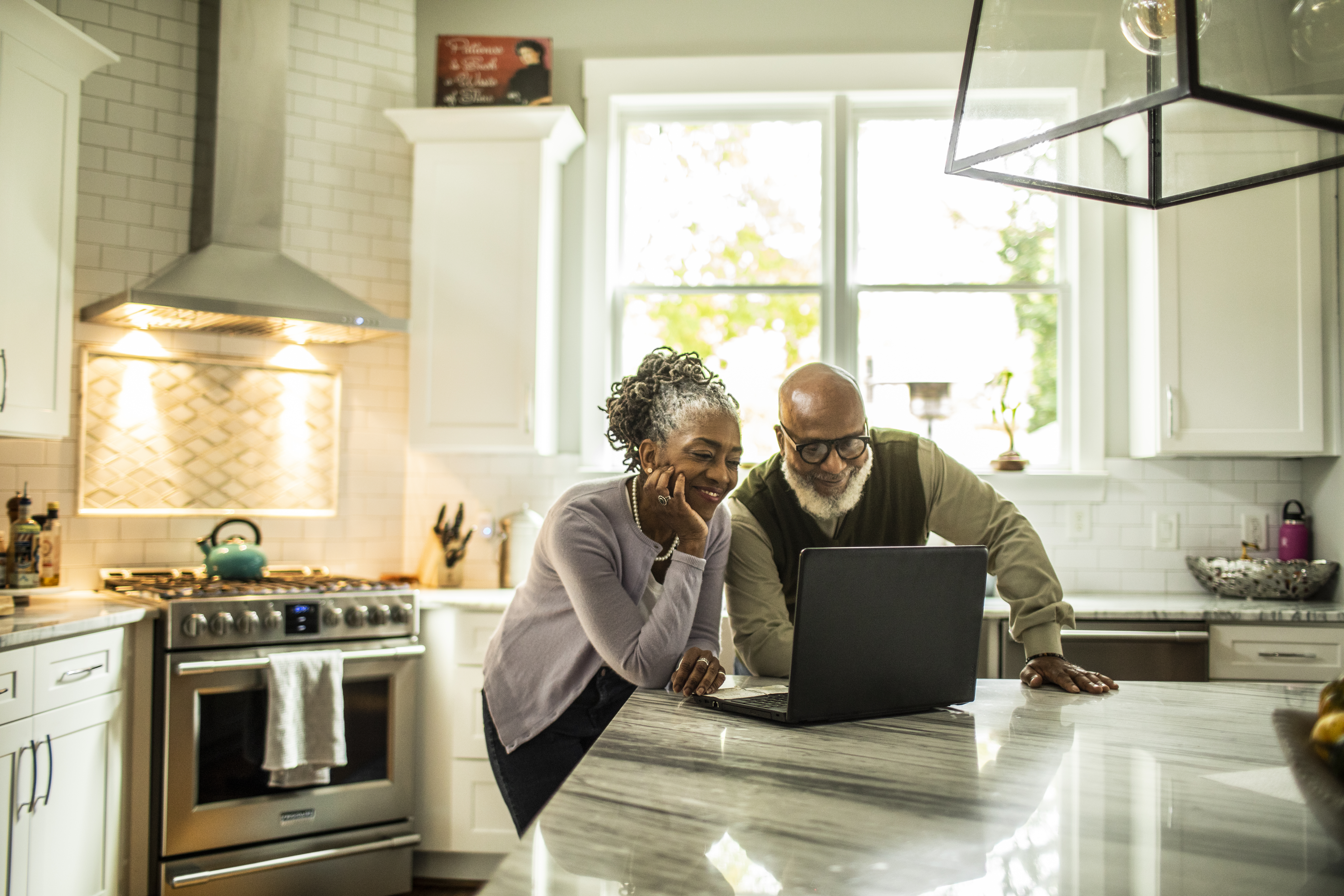 Couple Stands at the Kitchen Counter Viewing a Laptop