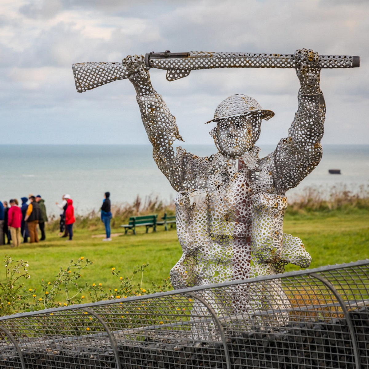 A soldier sculpture at the Arromanches D-Day Garden, with a group in the background