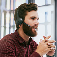 Male insurance agent wearing a headset, in a meeting, sitting in front of a computer screen.