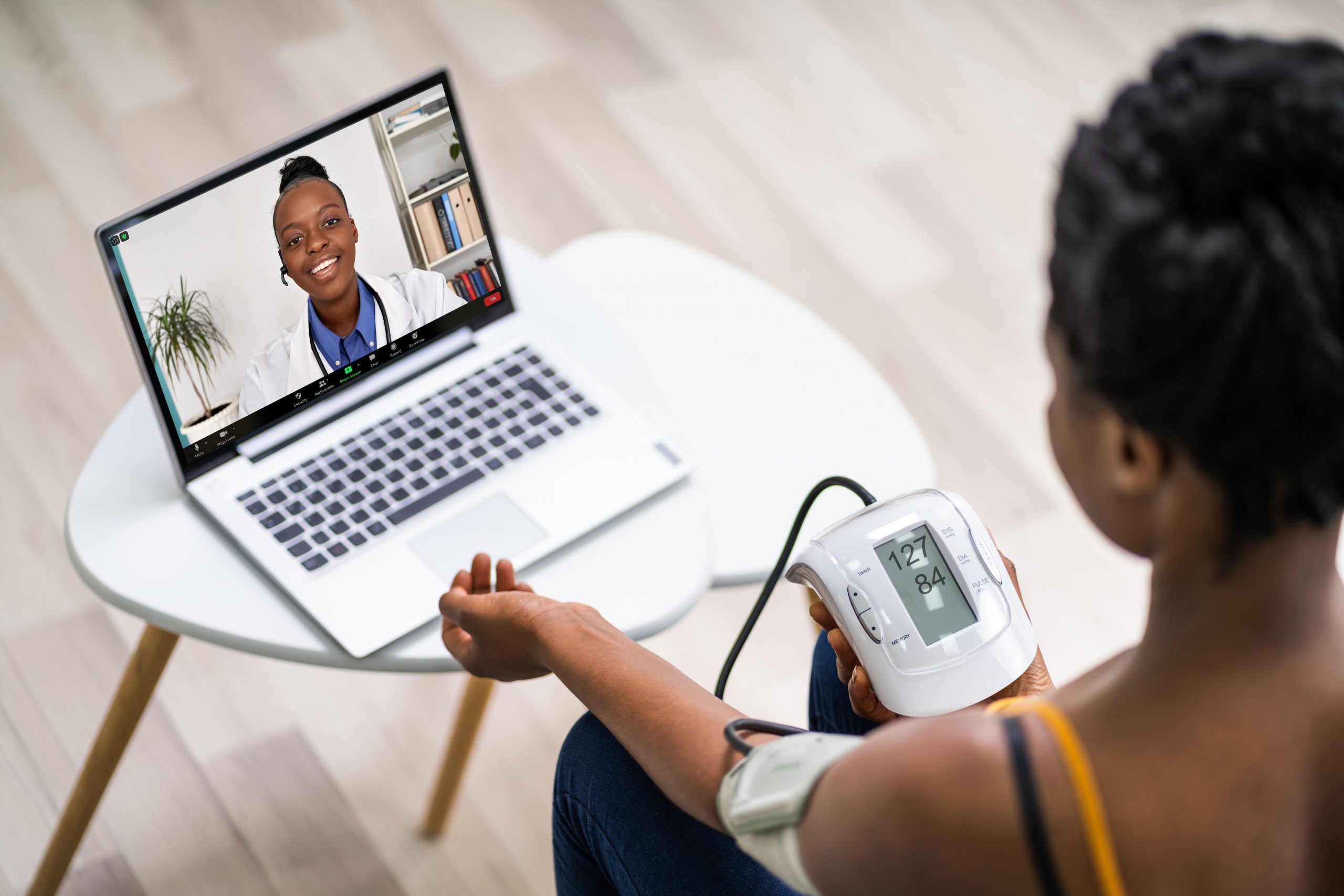 Woman measuring her blood pressure and video conferencing with a doctor in front of a laptop for telehealth appointment.