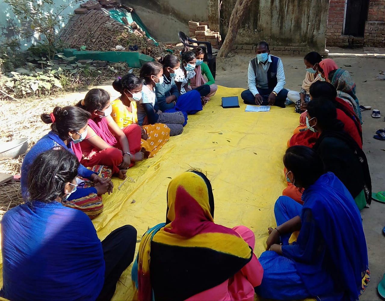 A group of youth sitting with an adult teacher on the ground in a village in India